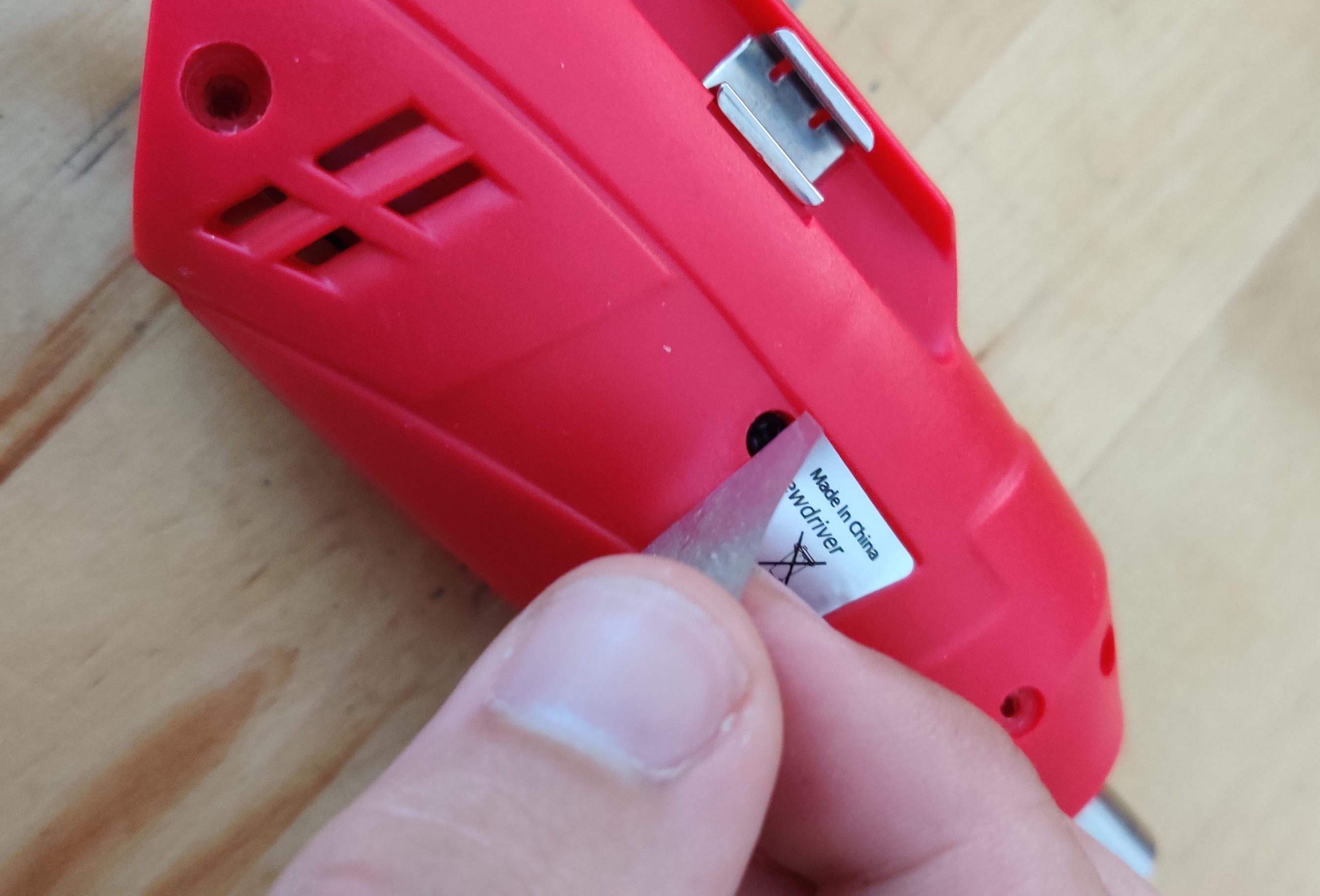 A screw hiding under a sticker on the cordless screwdriver